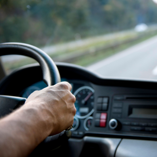 Hands on a steering wheel of a vehicle driving down the road.